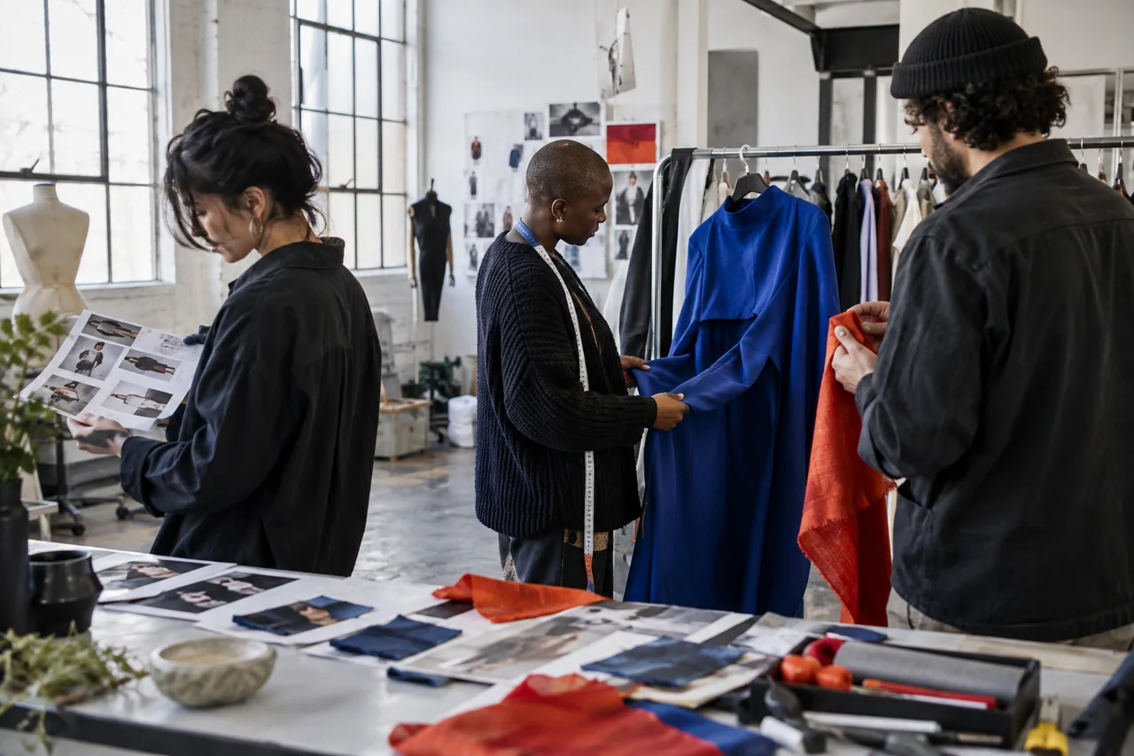 Creative practitioners reviewing cobalt clothing and fabric samples in a contemporary fashion studio.
