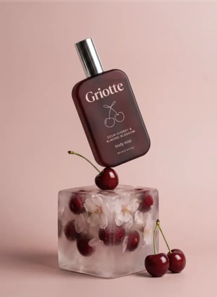 Griotte bottle balanced above a cherry-filled glass on a pink background
