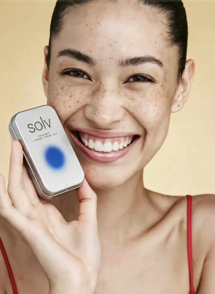 Smiling model holding a Sol skincare product against a warm yellow background